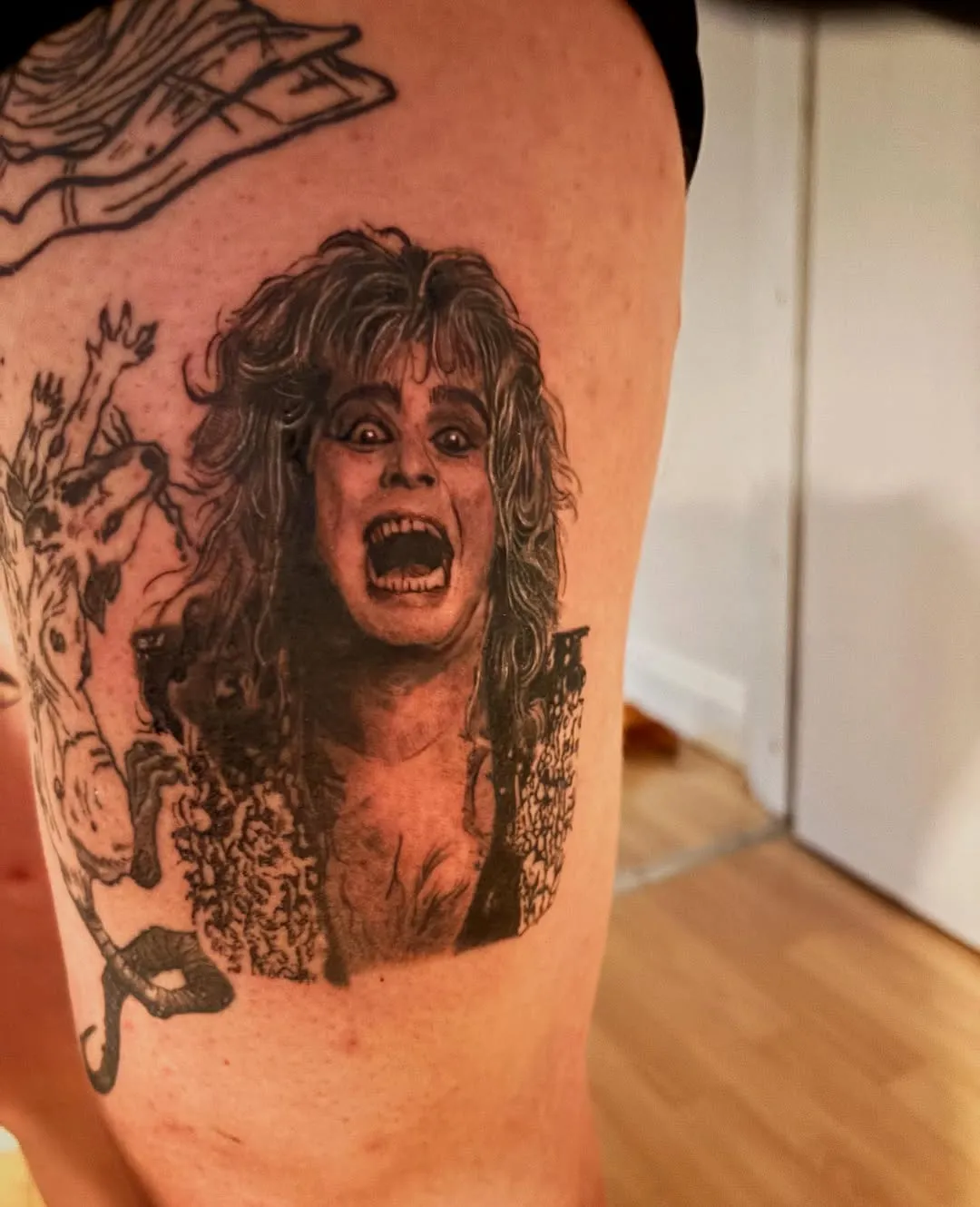 Detailed black & grey portrait of Ozzy Osbourne on the thigh, surrounded by illustrative figures.