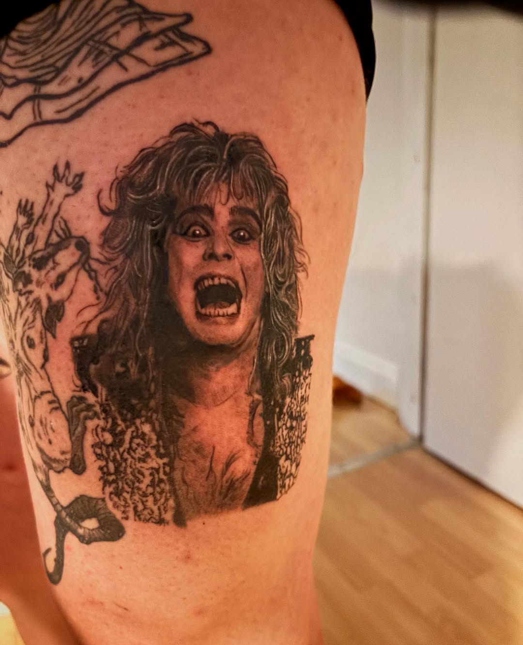 Detailed black & grey portrait of Ozzy Osbourne on the thigh, surrounded by illustrative figures.